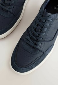Dunkelblaue Leder- und Wildledersneaker mit Schnürdesign, perforiertem Zehenbereich und weißer Gummisohle. Subtiler Steppstich an der Seite.