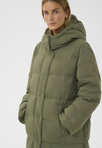 Polstret parka i olivengrøn, med høj krave, fortil trykknapper og to sidelommer. Glat struktur med en mat finish.