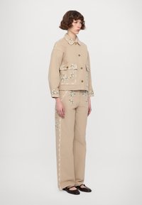 Beige cotton jacket and pants set featuring floral embroidery, decorative stitching, and gold buttons. Pockets on jacket and pants are visible.