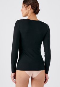 Zwart longsleeve top met een gladde textuur en een iets wijde halslijn, gecombineerd met een lichtgekleurde broek. De pasvorm is strak om het lichaam.