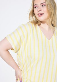 Blouse à rayures en V, avec des rayures verticales jaunes et blanches, à manches courtes et à coupe décontractée. Fabriquée en tissu léger et respirant.