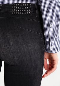 Svarta denimjeans med nitar på midjan, i kombination med en blå och vit rutig skjorta. Slät textur och slim fit.