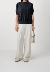 Top negro de manga corta con un ajuste holgado y dobladillo acanalado, combinado con pantalones de pierna ancha en beige claro y calzado de color claro.