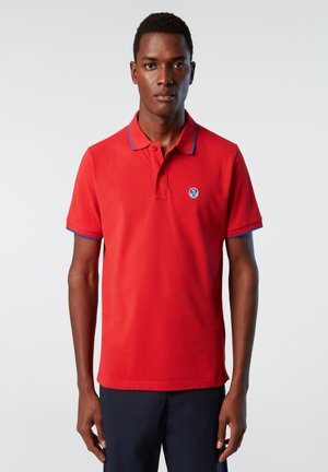 Maglietta polo rossa con dettagli blu su colletto e maniche, caratterizzata da un logo rotondo sul lato sinistro del petto. Realizzata in tessuto di cotone testurizzato.