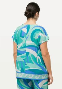 Top de manga corta en turquesa y azul con patrones abstractos de olas, que presenta un escote en forma de U y aberturas laterales para mayor libertad de movimiento.
