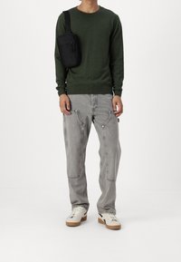 Maglione a maglia verde, pantaloni in denim grigi con dettagli sulle tasche, borsa a tracolla nera, scarpe bianche con suole beige, vestibilità casual, design minimalista.