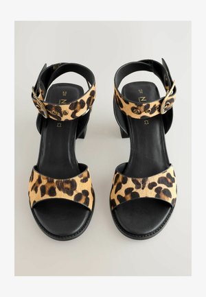 Leopardimustriga kontsaga sandaalid mustade nahkrihmade ja reguleeritava pannalaga. Omab plokkkontsa ja sujuvat sisereda.