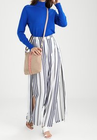 Maglione blu a collo alto, pantaloni a gamba larga bianchi e blu navy a righe con spacchi laterali, borsa a tracolla beige con accenti decorativi rosa, sandali bianchi.