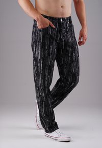 Schwarz- und graunare gestreifte Hose aus strukturiertem Material, mit lockerem Schnitt, Knopfverschluss und Seitentaschen, kombiniert mit weißen Sneakers.