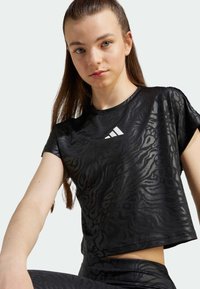 Top corto negro con un patrón de cebra texturizado, mangas cortas y un logo de adidas en blanco en el pecho. Acabado de tela suave.