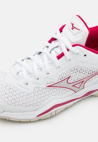 Biały but sportowy z siateczkową cholewką, czerwonymi akcentami i srebrnym logo. Charakteryzuje się misterną fakturą i tradycyjnym systemem sznurowania.