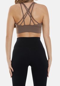 Brun sportbh med korsade band på ryggen, tillsammans med högmidjade svarta leggings, slät textur och åtsittande design.