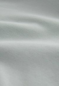Tissu gris clair avec une texture lisse, présentant un léger stretch et des plis ondulés, mettant en avant une couleur uniforme et une apparence douce.