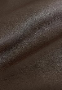 Texturált barna bőr, szemcsés felülettel, enyhe ráncokkal és redőkkel, hangsúlyozva rugalmasságát és gazdag színmélységét.