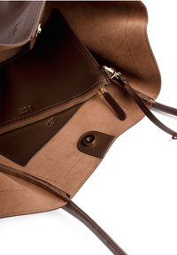 Interior de un bolso de hombro de cuero marrón con un gran bolsillo, un compartimento con cremallera y un cierre de botón. Textura suave con costuras limpias.