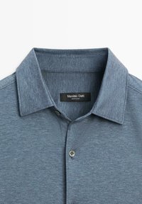 Polo shirt blu con colletto realizzato in un tessuto texturizzato, con un'apertura a bottoni e un'etichetta che recita "Massimo Dutti."