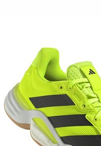 Zapato deportivo brillante de color verde neón con parte superior de malla, detalles en negro y media suela blanca. Cuenta con un cuello acolchado y superficie texturizada.