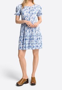 Vestido floral azul con mangas cortas abullonadas, dobladillo en capas y tejido ligero. Combinado con mules de tacón marrón con tachuelas plateadas.