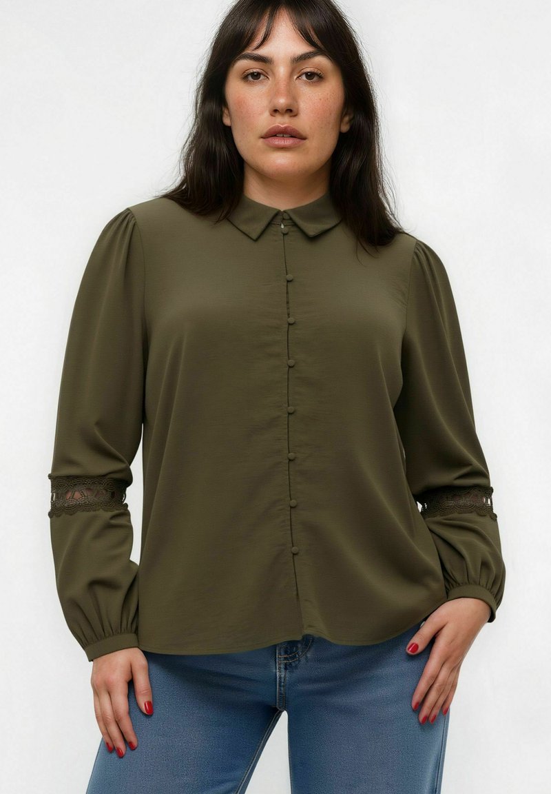 Blouse vert olive avec col, fermeture à boutons sur le devant et manches longues avec des accents en dentelle aux poignets. Tissu lisse avec une coupe décontractée.