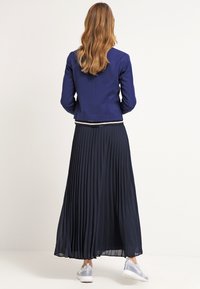 Granatowa kurtka o dopasowanym kroju, zestawiona z plisowaną granatową spódnicą maxi. Dopełnieniem stroju są białe trampki. Widoczny teksturowany materiał.