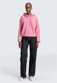 Roze hoodie met een ontspannen pasvorm, gecombineerd met donkerblauwe wijde spijkerbroeken en witte sneakers. Eenvoudig ontwerp zonder zichtbare patronen.