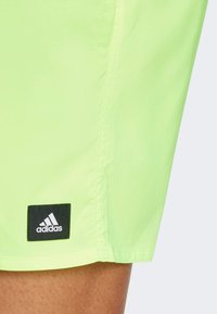 Pantaloncini verde neon realizzati in materiale leggero, con toppa con logo Adidas nero e tasche laterali sulle cuciture.
