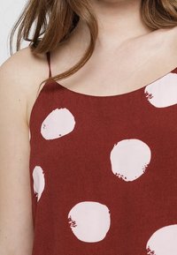 Top senza maniche in terracotta con grandi motivi circolari rosa. Presenta spalline sottili e una superficie di tessuto liscia.