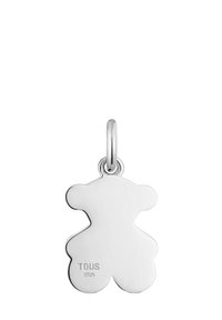 Ciondolo a forma di orsetto in argento, finitura lucida con bordi lisci, dotato di anello per il fissaggio. Inciso con "TOUS" e "S925" su un lato.