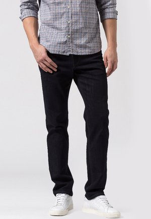 Dunkelblaue Jeans mit geradem Schnitt, aus Denim gefertigt, mit minimaler Naht und klassischem Design. Kombiniert mit weißen Sneakern.