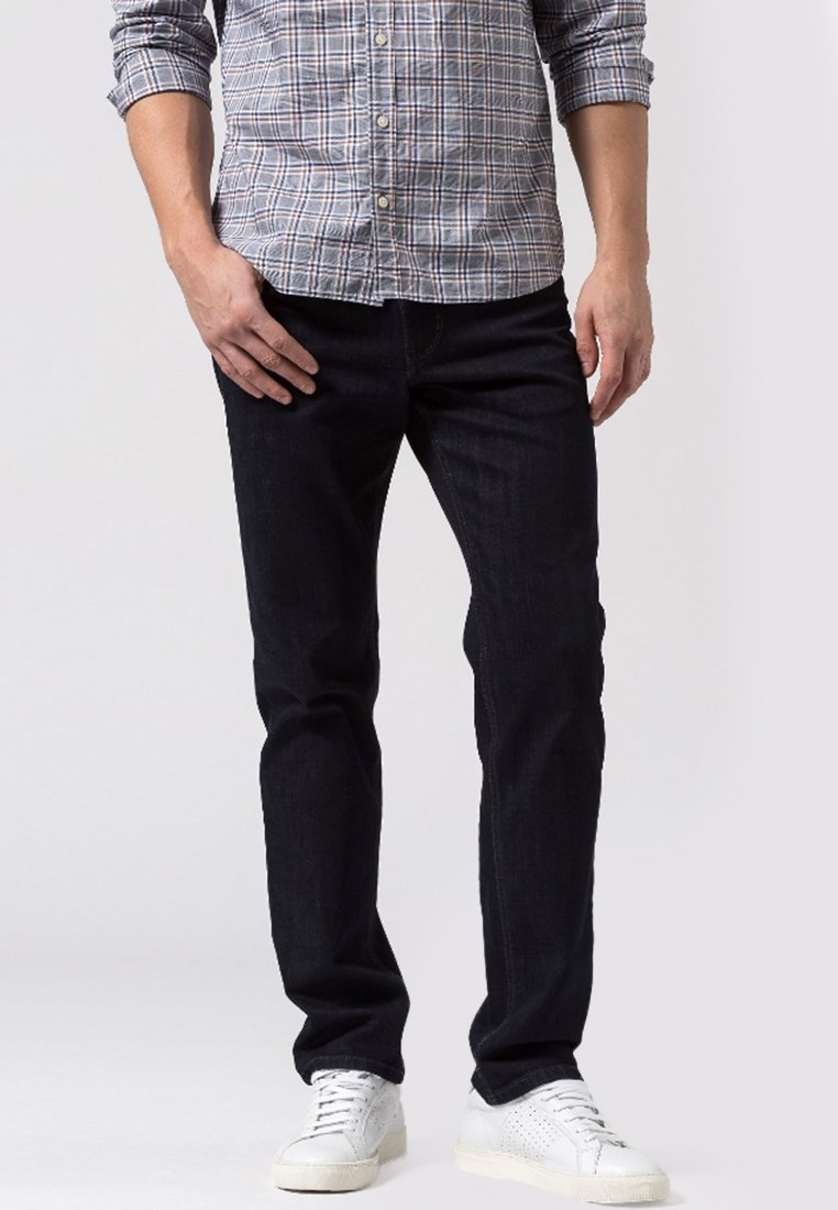 Vaqueros azul oscuro de corte recto, hechos de denim, con costuras mínimas y un diseño clásico. Combinados con zapatillas blancas.