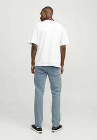 Tricou alb supradimensionat cu un guler din bandană roșie închisă, blugi bleu deschis și teniși negri cu talpă joasă, văzuți din spate.