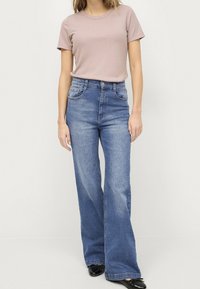 Jasnoróżowy, prążkowany t-shirt w połączeniu z wysokimi, dzwonowymi niebieskimi dżinsami. Gładka faktura, standardowe szwy i brak widocznych wzorów.