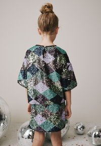 Paljettklänning med ett diamantmönster i grönt, lila och svart. Kortärmad, lös passform och en ringning med öppning bak.