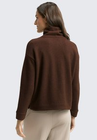 Pull en tricot marron avec un col montant et une coupe ample. Présente des épaules tombantes et des manches longues, avec des poignets et un ourlet côtelés.