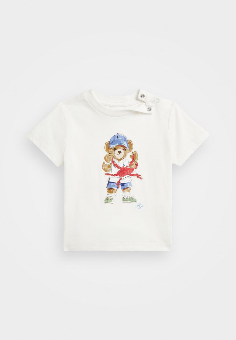 T-shirt bianca a maniche corte con una grafica colorata di un orso di peluche che indossa un cappellino blu, scarpe verdi e tiene un'aragosta. Dettaglio con bottoni a pressione.