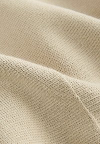 Béžová pletenina s texturovaným vzorem, která má měkký a mírně chlupatý povrch. Materiál se zdá být lehký a ohebný.