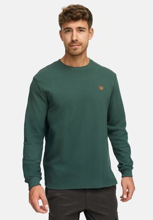 Grønn langermet skjorte med ribbet tekstur, rund hals og et lite brunt logo-merke på brystet. Har tettsittende mansjetter og hem.