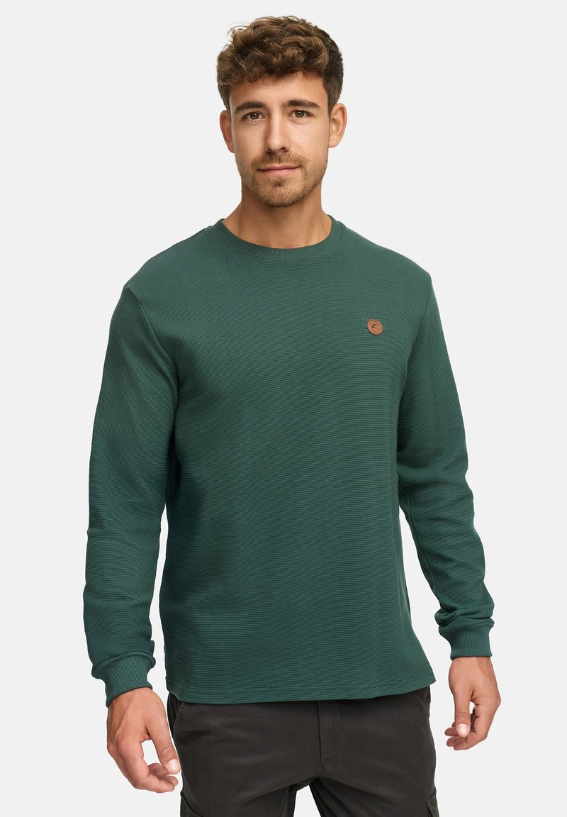 Grünes Langarmshirt aus geripptem Material, mit Rundhalsausschnitt und einem kleinen braunen Logopatch auf der Brust. Verfügt über eng anliegende Bündchen und Saum.