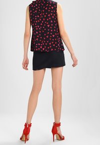 Zwarte mouwloze top met een rood hartpatroon, gecombineerd met een zwarte rok en rode hoge hakken met ruffles en ritsen.