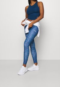 Canotta sportiva blu navy abbinata a leggings aderenti con una base blu e motivi geometrici colorati. Sneakers bianche completano l'outfit.