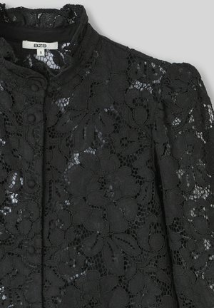 Tissu en dentelle noire avec motif floral, col montant et fermeture à boutons. Surface texturée avec des éléments transparents contrastants.