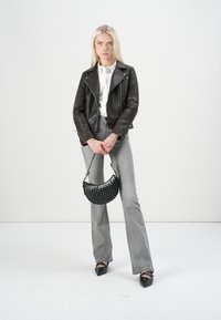 Svart skinn bikerjakke med sølvdetaljer, kombinert med grå flared jeans og en svart naglet håndveske. Modellen har på seg svarte spisse sko.