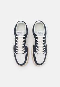 Granatowe zamszowe sneakersy z białymi skórzanymi akcentami, okrągły czubek, perforowane wstawki na czubku, oraz kremowe sznurówki. Etykieta marki widoczna na języku.