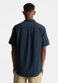 Korte mouwen, donkerblauw shirt in textuurstof, met een rechte zoom en een plooidetail aan de achterkant. Casual ontwerp, relaxed fit.