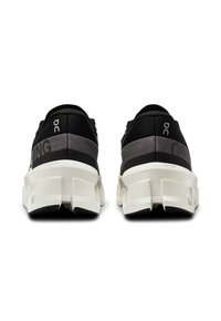 Un paio di scarpe sportive nere e grigie viste da dietro, con suole spesse bianche segmentate e il marchio "ON" sui talloni.