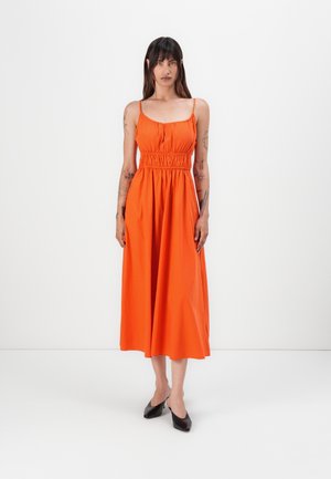 Orange midi dress with a fitted bodice, elastic waistband, and thin straps. Smooth fabric with a flowing, flared skirt. Black shoes.