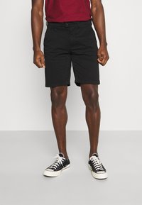 Sorte bomullsshorts med vanlig passform, med knappeåpning, to frontlommer og rullet kant. Sammen med sorte joggesko.
