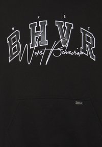 Černá mikina s kapucí, na které jsou velká bílá vyšitá písmena "BHVR" nad textem "Worst Behavior" napsaným kurzívou. Je zde přítomná kapsa na přední straně.