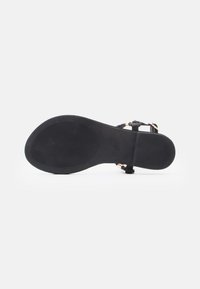 Juodas šleputės padas, pagamintas iš gumos medžiagos, plokščias dizainas, tekstūruota paviršius ir plonos dirželiai, sujungti auksiniu akcentu.