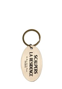 Llavero de latón con una etiqueta ovalada. El texto grabado dice "SCALPERS LA RÉSIDENCE 8 Rue de la Tour PARÍS" en negrita de color negro.